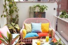 a small bright balcony with a pink loveseat, a small table, a white bench with storage, potted greenery and bright pillows