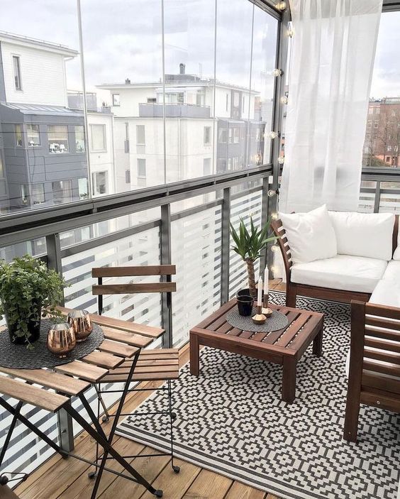 a small contemporary balcony with a geo rug, simple stained furniture and some greenery