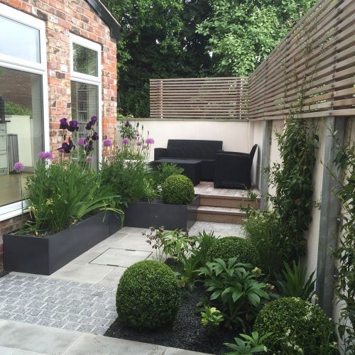 a small contemporary terrace with dark furniture, potted greenery and blooms and wooden screens for privacy
