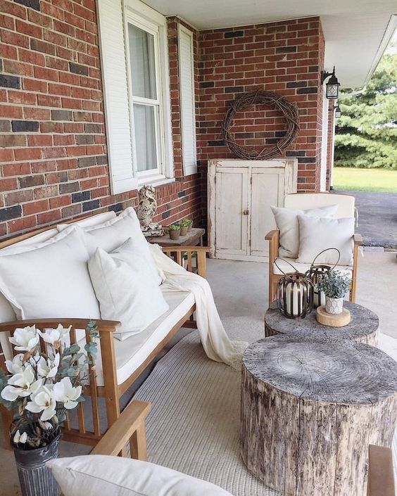a small farmhouse terrace with neutrla upholstered furniture, tree stumps as side table and potted greenery and blooms
