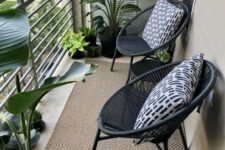 a small modern balcony with a jute rug, black chairs and pillows and some potted tropical plants
