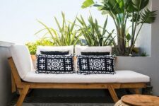 a small modern balcony with a tropical feel, with a lounger and printed pillows, a wooden coffee table and potted plants