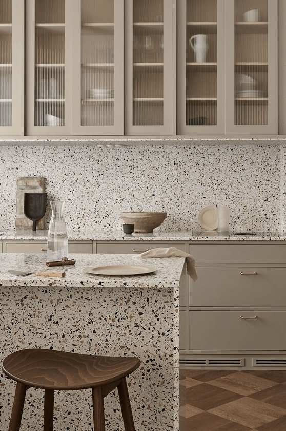 a sophisticated greige kitchen with flat panel and glass cabinets, white terrazzo countertops and a backsplash
