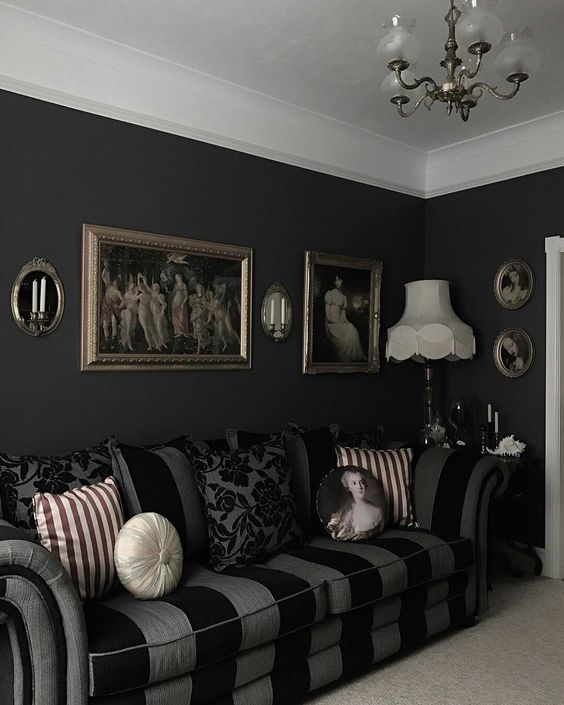 a stylish Gothic living room with black walls, a striped sofa, artworks, a chandelier and printed pillows