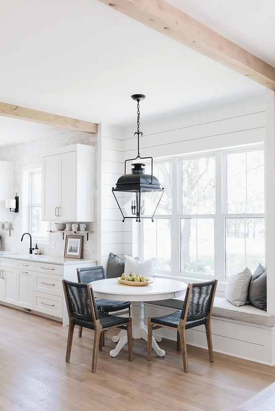 a stylish farmhouse kitchen with planked walls and shaker cabinets, a windowsill bench and a round table plus black chairs