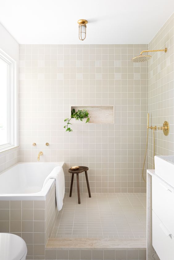 a stylish modern bathroom clad with square grey tiles, a bathtub clad with them, too, a white vanity with a white sink and gold touches