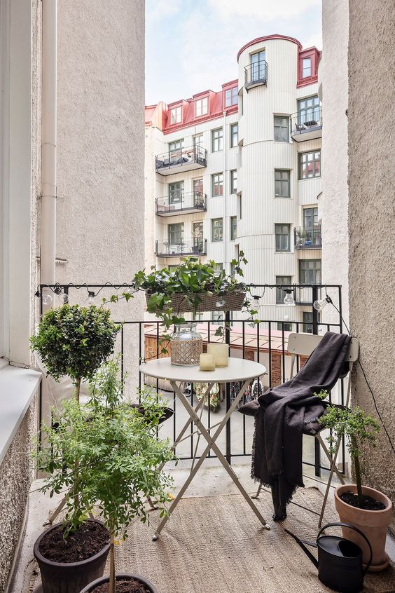a tiny and elegant balcony with delicate folding furniture, potted plants and candles is a cool and chic space