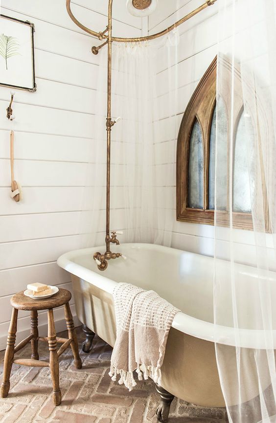 a vintage farmhouse bathroom with beadboard on the walls, a tan vintage tub, a wooden sotol, brass touches and a mirror in a wooden frame
