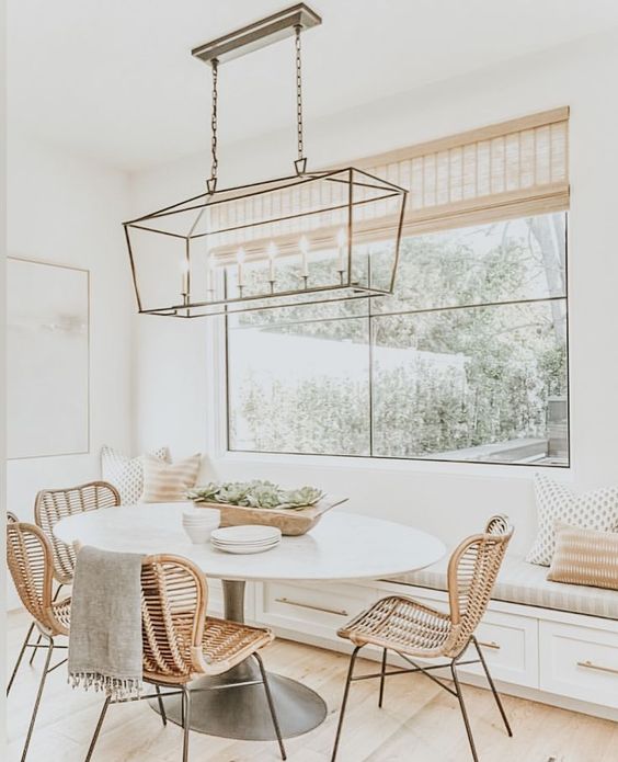 A welcoming modern farmhouse neutral dining space with a built in bench, an oval table, rattan chairs, a chic brass pendant lamp