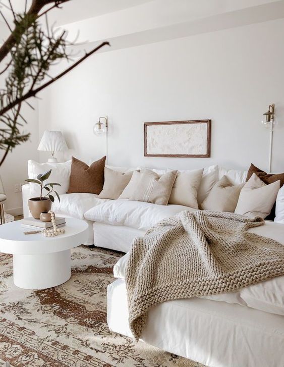 a welcoming neutral living room with a large white sectional, lots of mismatching pillows, a round coffee table and some branches for decor