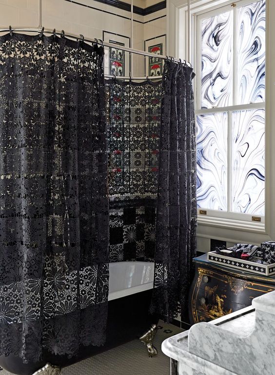 a whimsy Gothic bathroom with black and white mosaic tiles, a black vintage bathtub and a black lace curtain, marble glass and a marble vanity