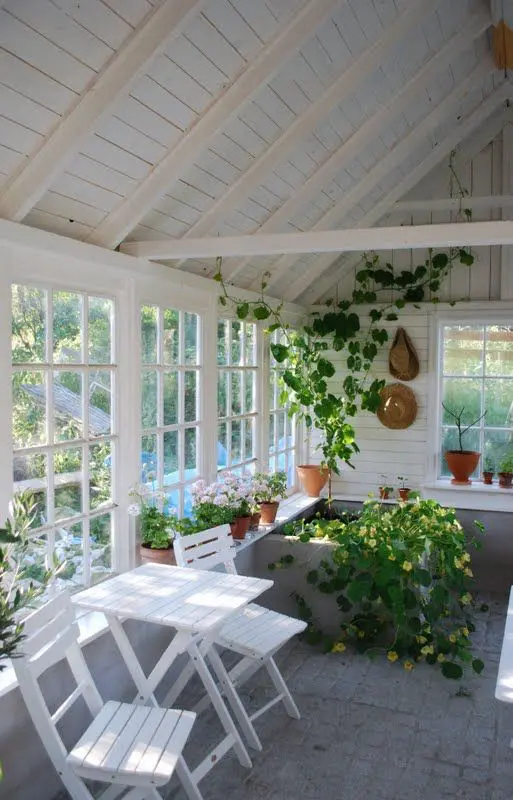 a white Scandi sunroom with a white dining set, lots of greenery and blooms is a cozy space to have a drink