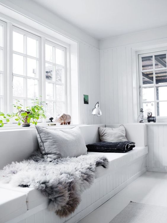 a white Scandinavian sunroom with a built-in bench, pillows and faux fur, potted greenery and lamps is amazing