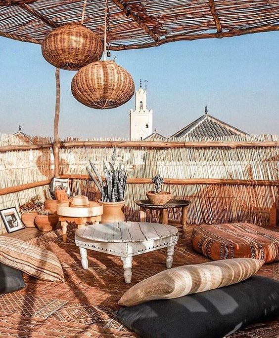 An earthy colored boho terrace with layered rugs, pillows and cushions, low coffee tables, woven pendant lamps