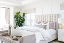 an elegant neutral bedroom with a creamy bed, neutral and pastel bedding, a pastel bench and a statement plant