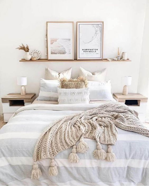an ethereal neutral bedroom with wooden nightstands, a bed, an open shelf, pampas grass and artworks