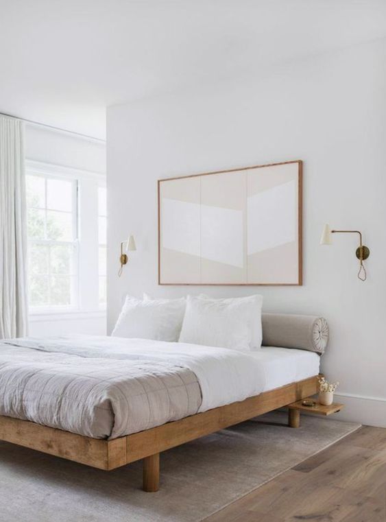 an etherel neutral bedroom with a wooden bed, neutral bedding and an oversized artwork plus sconces