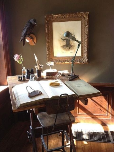 a Gothic Victorian home office with grey walls with paneling, a small desk and a vintage stool, a statement artwork, a raven and a retro metal desk lamp