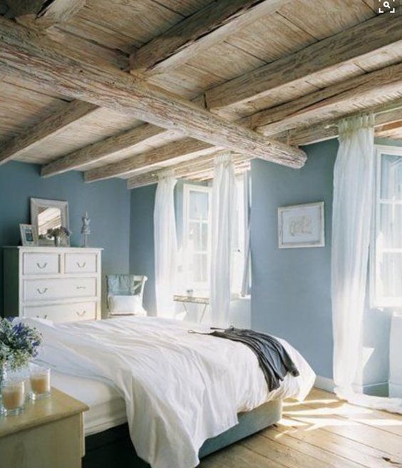 a blue bedroom with wooden beams on the ceiling, neutral furniture, artworks and some blooms