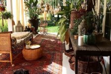 a boho porch with a rattan bench, a lot of baskets, a printed boho rug, woven lanterns and much greenery
