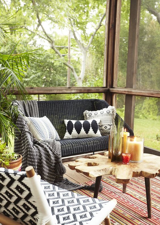a boho screened porch with woven and wooden furniture, printed textiles, a wood slice rug and potted greenery