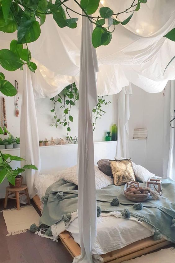 a boho spring bedroom in neutrals with a bed on the floor, pastel bedding, potted greenery
