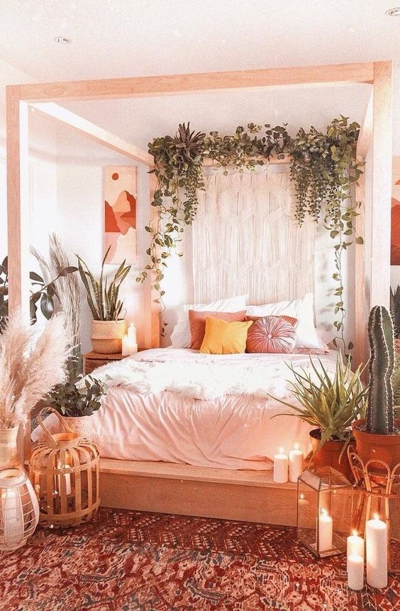 a boho spring bedroom in neutrals, with a wooden canopy bed, potted plants, macrame, candles and a boho rug