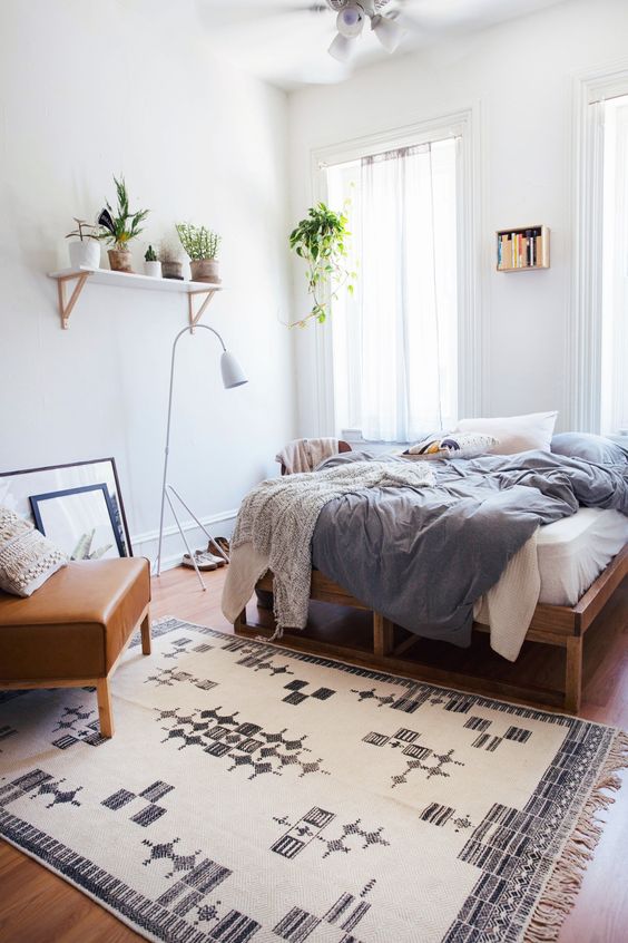 a boho spring bedroom with a wooden bed, a leather chair, blue and white bedding, a printed rug, potted greenery