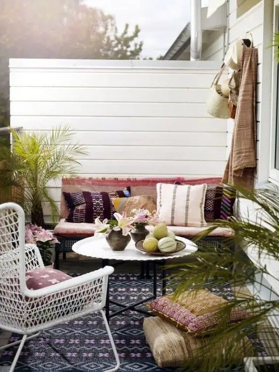 a boho spring terrace with colorful textiles and rugs, potted greenery and a white wicker chair