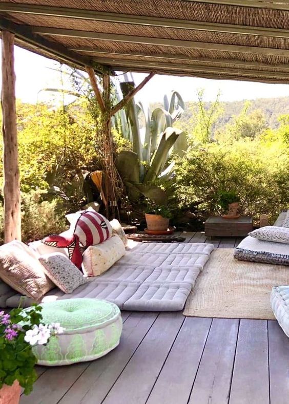 a boho terrace with cushions and pillows, potted greenery and statement plants plus colorful pillows