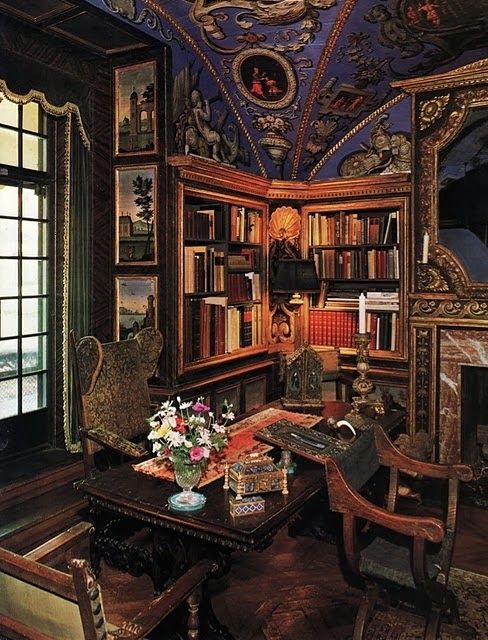 A bold Gothic revival home office with built in bookshelves, a heavy carved wooden and chairs, bold artworks and a gorgeous lilac ceiling with paintings