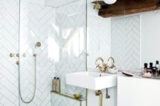 a bright glam white bathroom with chevron clad tiles, gilded touches, dark wooden beams and a square sink