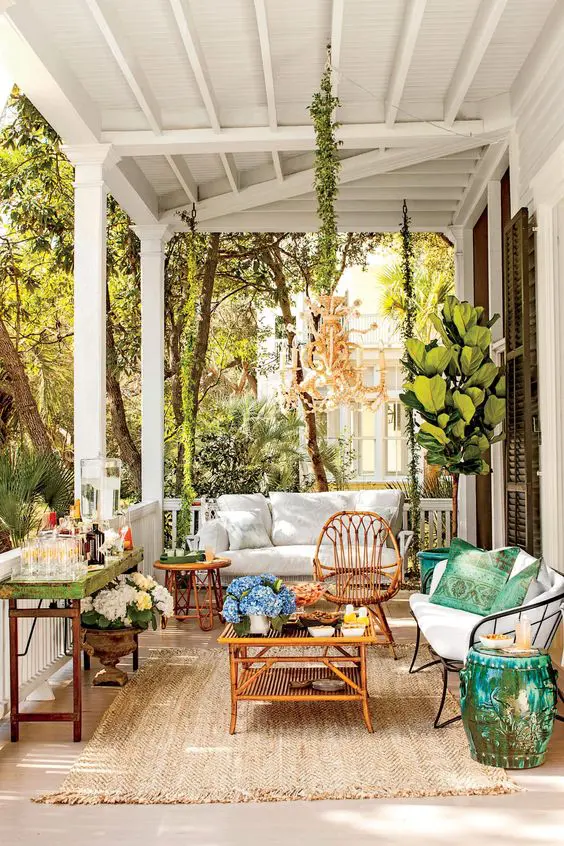 a bright porch with a sofa, rattan furniture, a metal daybed, a bar and lots of blooms and statement plants