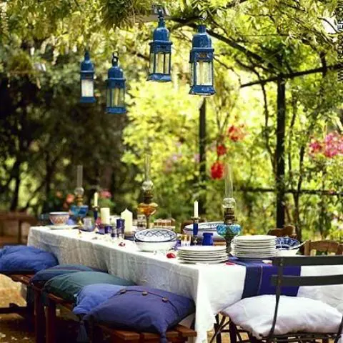 a bright spring terrace with bold linens, blue pillows, blue lanterns over the table and candles and plates
