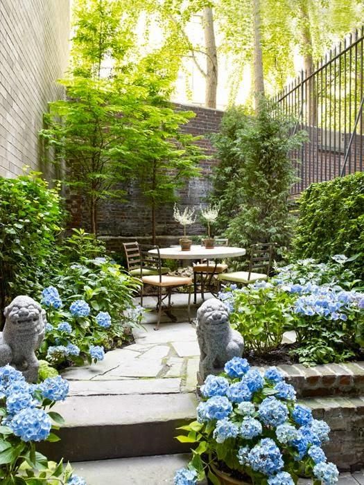 a bright spring terrace with greenery and blue blooms everywhere, with simple modern furniture and potted plants