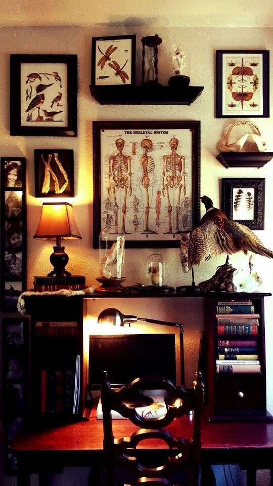 a chic Gothic home office with a desk with additional bookshelves, a vintage poster gallery wall, a heavy carved chair and a vintage table lamp