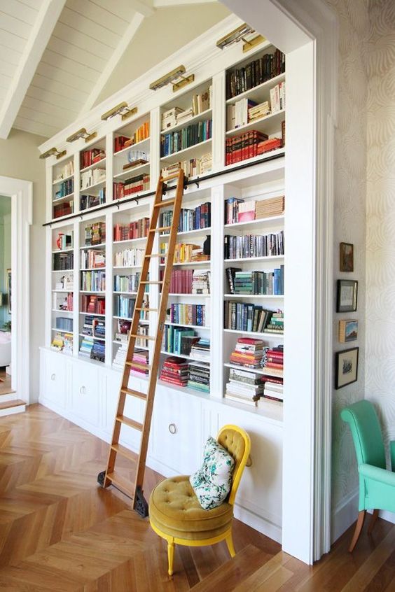 A chic built in bookshelf unit with a ladder, a mustard chair and additional lights is very chic