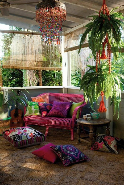 a colorful screened boho porch with a pink loveseat, colorful printed pillows, potted plants and a colorful glass chandelier