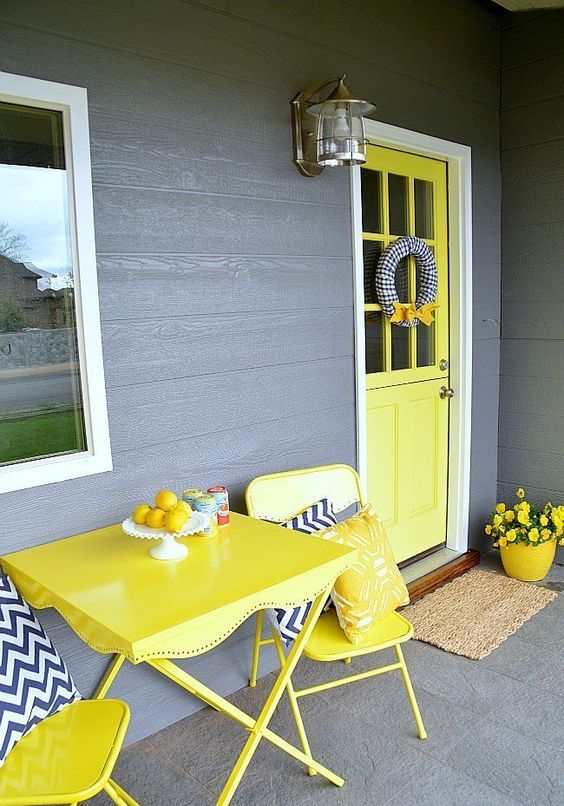 a colorful spring porch with yellow furniture, door and a pot plus blooms and chevron pillows