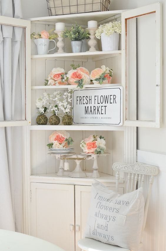 a corner bureau with fresh peachy and white blooms, candles, vine balls and an artwork