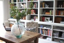 a dark built-in bookshelf with lots of books, wire baskets, greenery, figurines and other decor