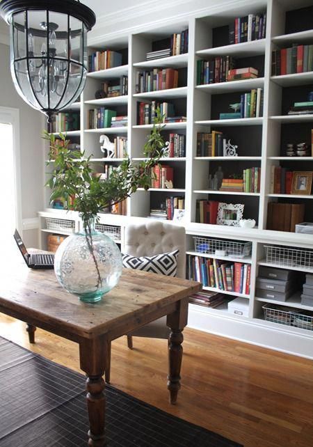 A dark built in bookshelf with lots of books, wire baskets, greenery, figurines and other decor