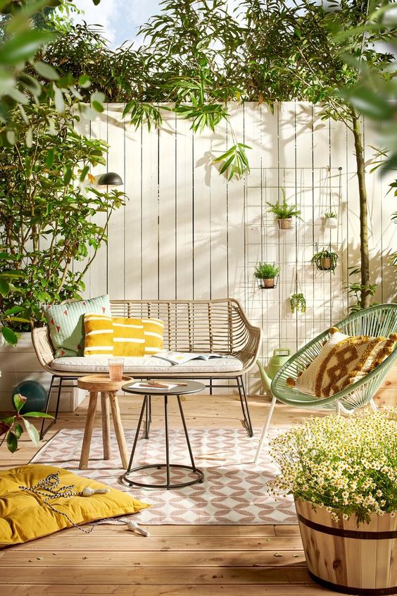a fresh and welcoming spring terrace with wicker furniture, potted greenery and blooms and touches of mustard and green