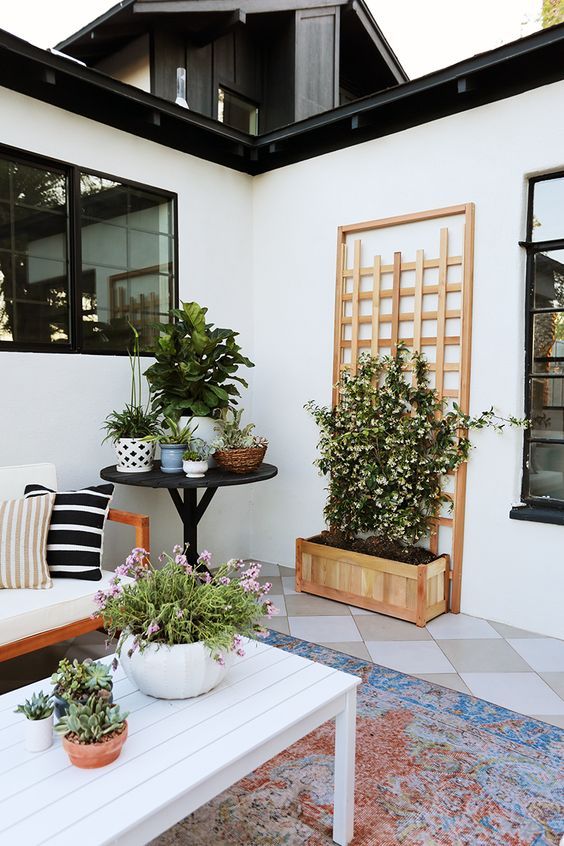 a fresh spring modern terrace with potted blooms and greenery, simple wooden furniture and printed pillows