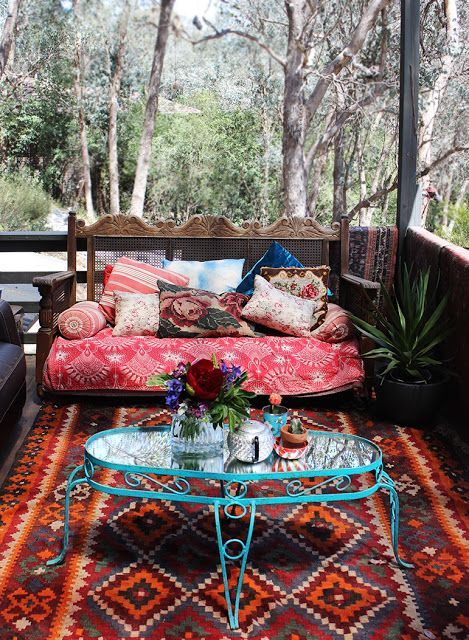 A gypsy styled porch with a bright printed rug, a colorful bench and a blue forged side table