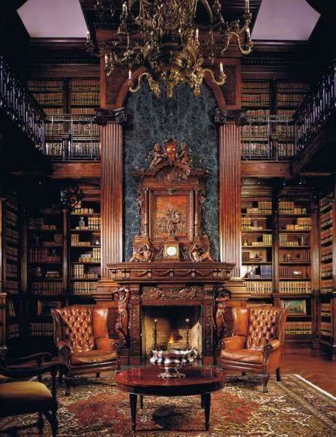 a large exquisite Gothic library with bookshelves covering all the walls up to the ceiling, a fireplace wiht a carved mantel, leather chairs and a refined chandelier