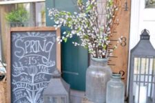 a lovely spring porch with a chalkboard sign, candle lanterns, churns with willow pussy and bright blooms