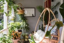 a lush boho porch with lots of greenery and blooms planted, a rattan hanging chair, a pritned rug is very cool