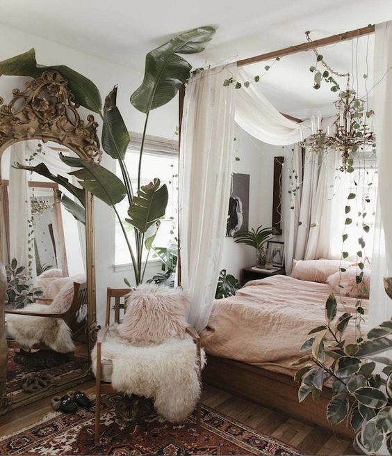 a messy boho spring bedroom with wooden furniture, pink bedding, a boho rug and lots of greenery and plants