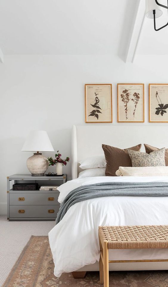 a mid-century modern bedroom with a grey nightstand, a woven bench, a white bed, grey and white bedding